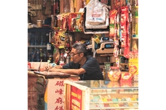 Image A man sitting in his store behind the counter surrounded by food and products.